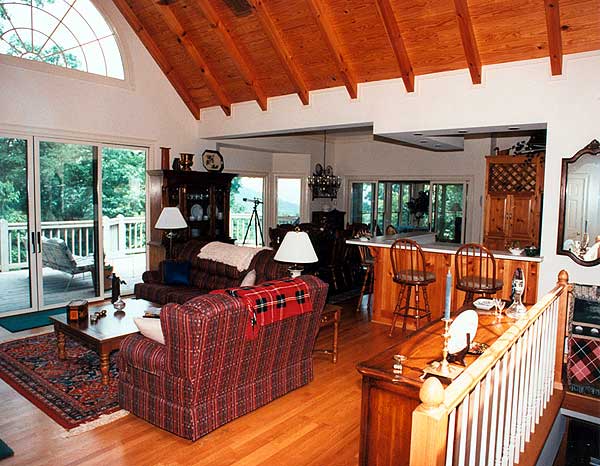 Living area with vaulted wood-beamed ceiling, large windows, deck access, and open bar.