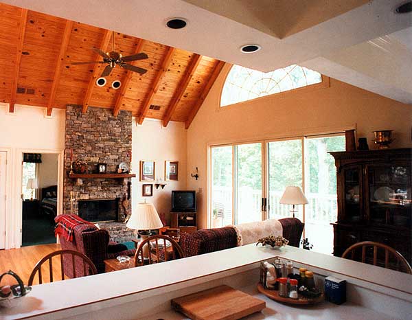 Interior view of great room with stone fireplace, vaulted wood-paneled ceiling, and large sliding glass doors.