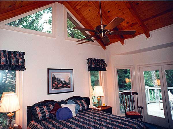 Bedroom with vaulted wood-paneled ceiling, triangular clerestory windows, ceiling fan, and French doors to deck.