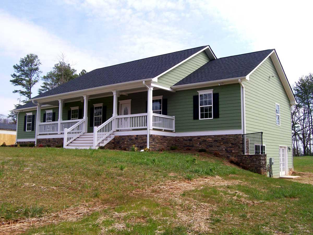 House plan exterior: Ranch style, full-width covered porch with white railings and steps, stone foundation, green siding.