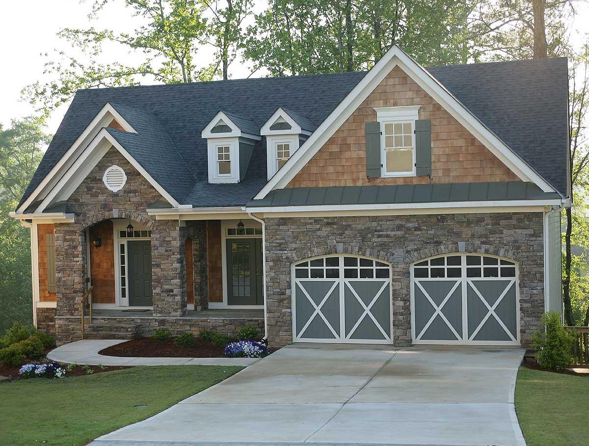 House plan exterior with stone facade, gable dormers, shingle siding, and a double garage with arched doors.