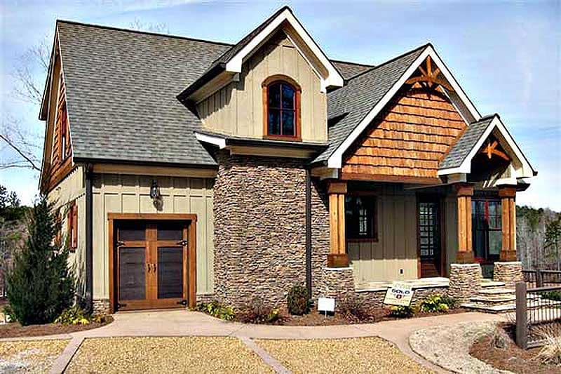 House plan exterior: Two-story home with stone accents, cedar shake gables, covered porch, and wooden garage door.