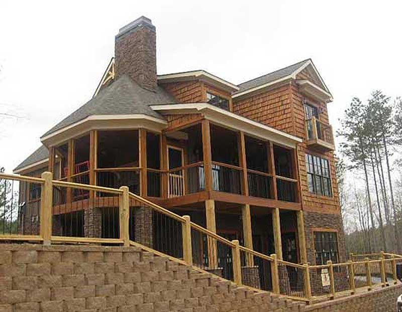 House plan exterior with stone base, wood siding, multiple levels of porches, and a prominent brick chimney.