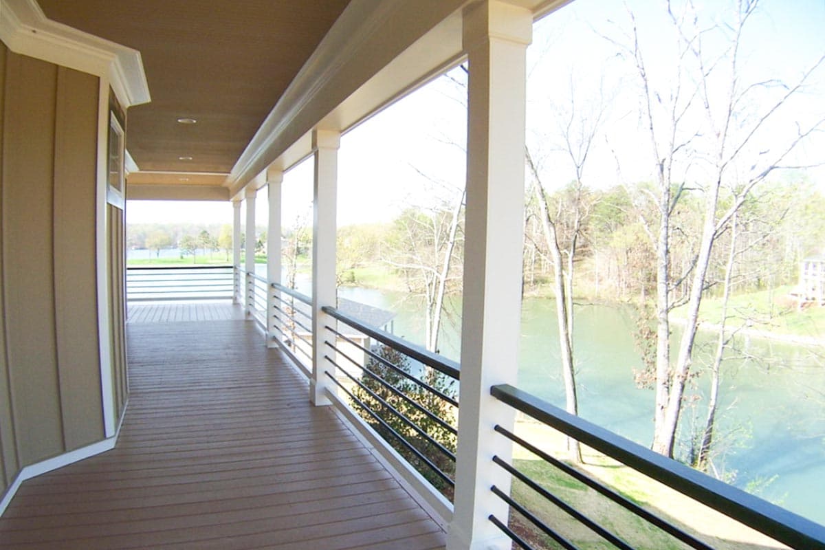 House plan exterior featuring a deep covered porch with white columns and metal railings overlooking a body of water.