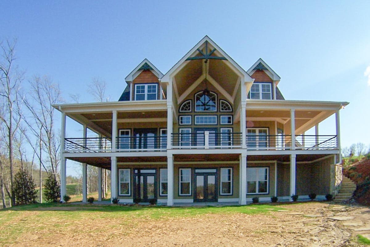 House plan exterior: Modern design with a full-length covered deck, a prominent central gable, and a large bank of arched and rectangular windows.