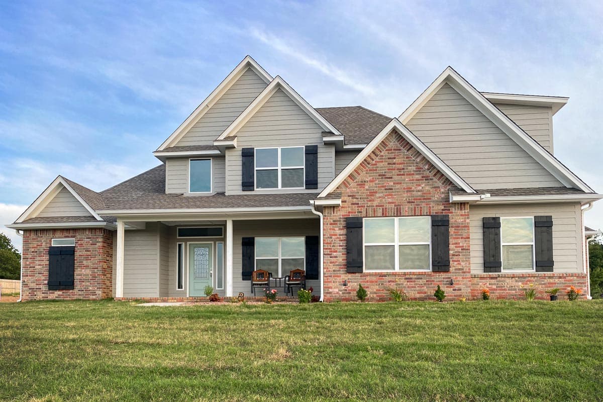 Two-story house plan exterior with gabled rooflines, brick and siding facade, covered front porch with columns, and dark shutters.
