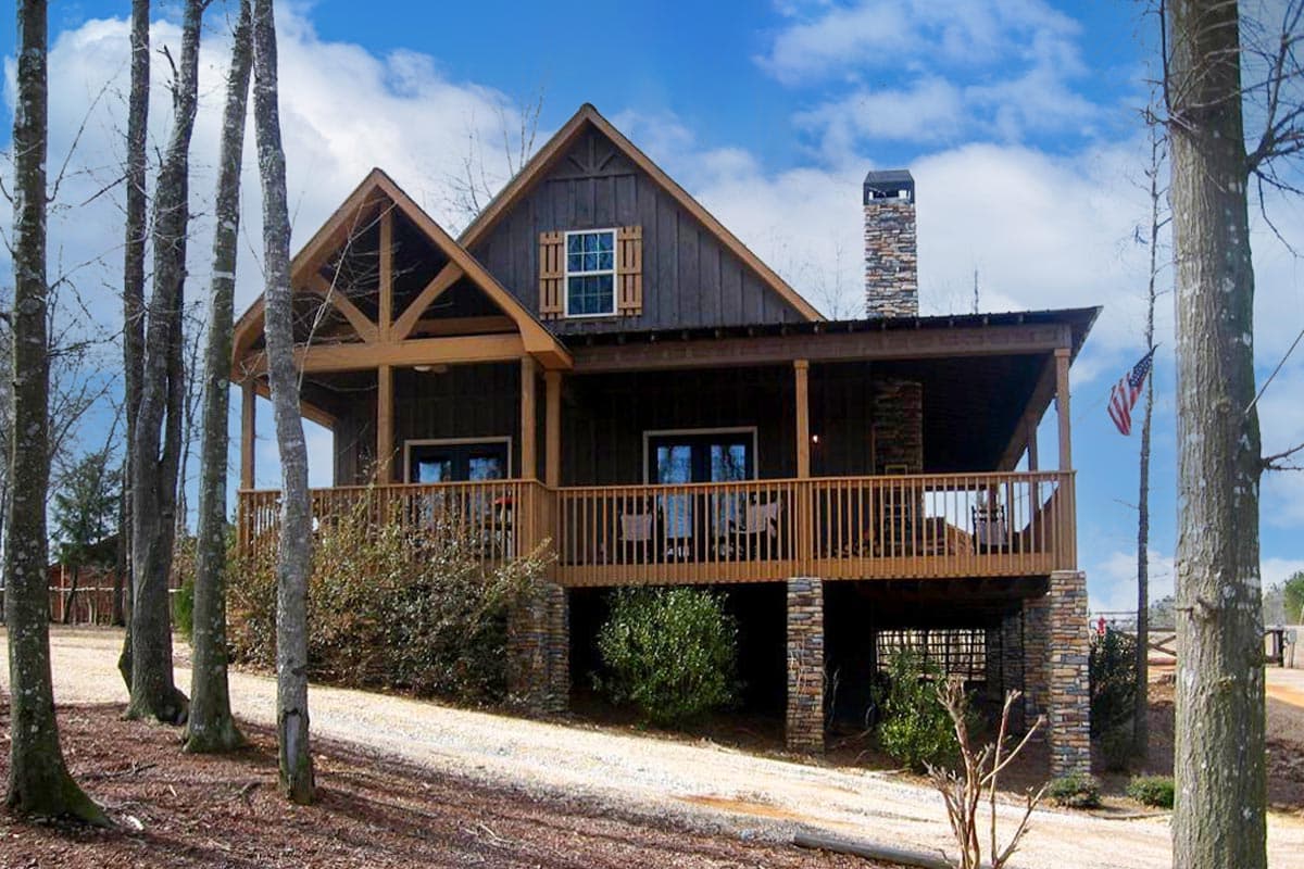 House plan exterior: two-story modern farmhouse with wrap-around porch, wood gables, stone chimney, and dark wood siding.