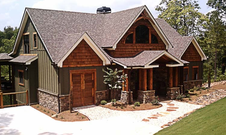 House plan exterior: Two-story home with timber accents, stone foundation, prominent gables, covered entry with stone columns, and a two-car garage.