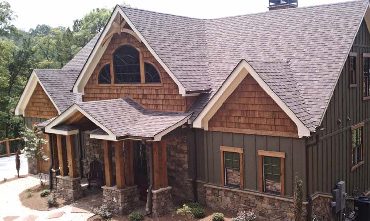 House plan exterior: Craftsman style, stone and wood siding, prominent gables, covered entry with timber posts, and arched dormer window.
