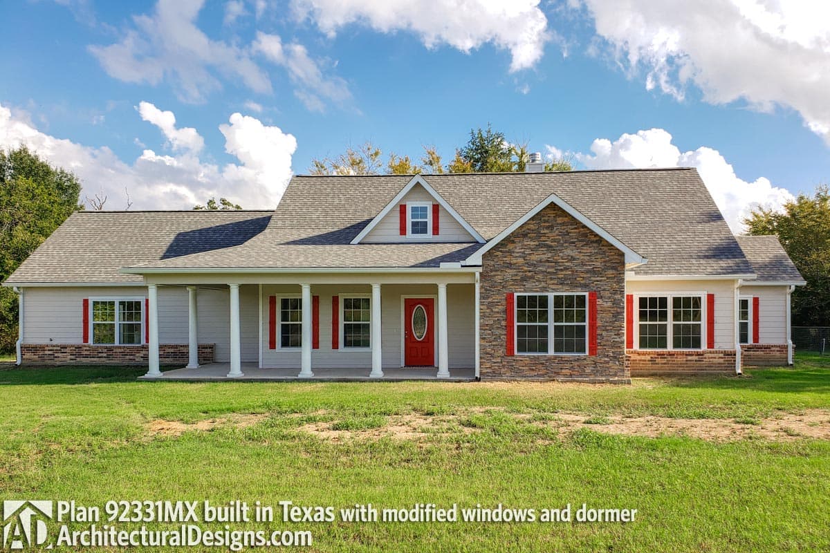 Ranch house plan exterior with stone facade, covered porch, dormer, and red shutters.