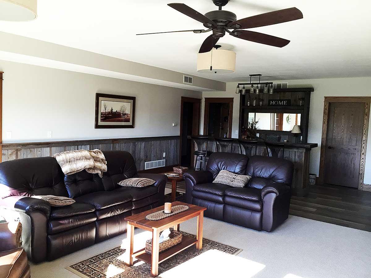 Interior view of a home entertainment space with leather sofas, a wooden bar with stools, and a ceiling fan.