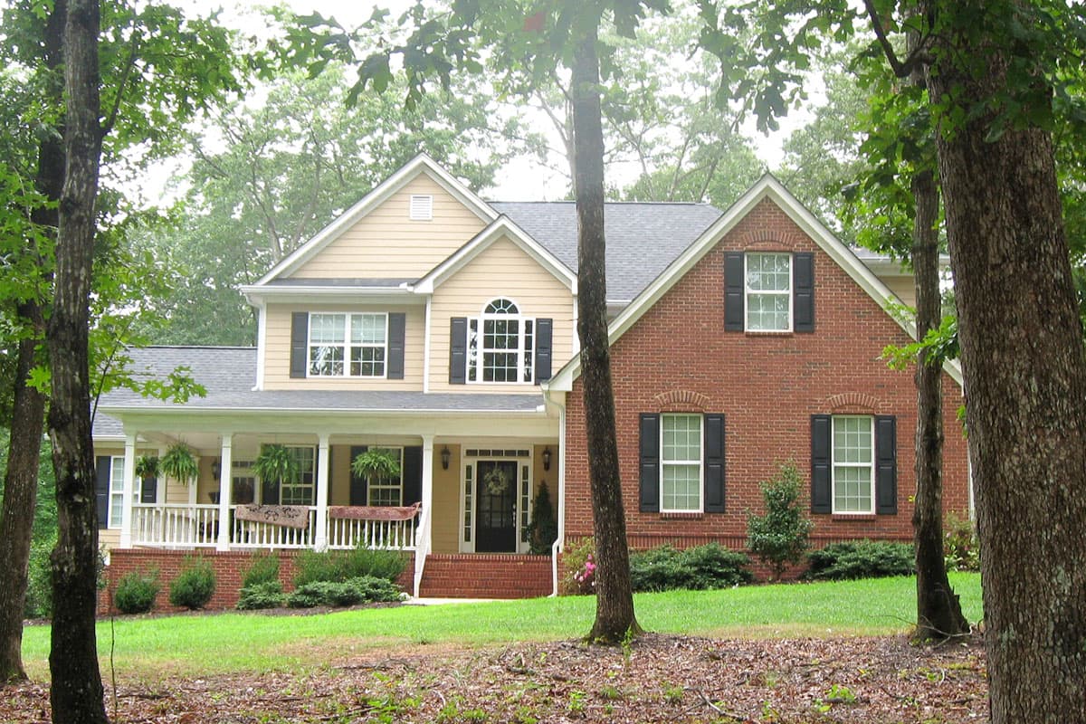 House plan exterior: Two-story home with partial brick facade, covered front porch, multiple gables, and arched window detail.