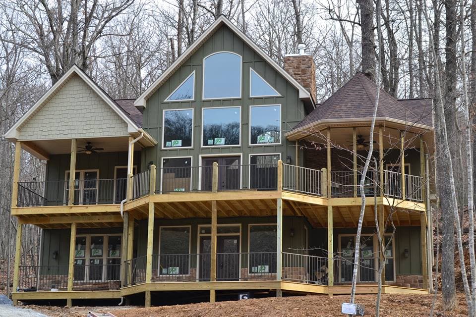 House plan exterior: two-story home with gabled roof, large front window array, covered porches, and multi-level decks.