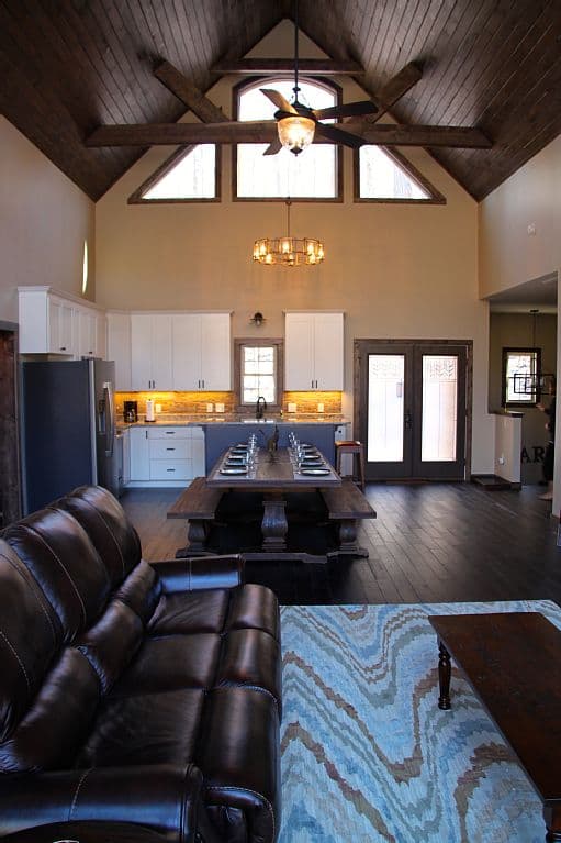 Great room with vaulted wood-beam ceiling, kitchen, dining area with farmhouse table, and leather sofa.