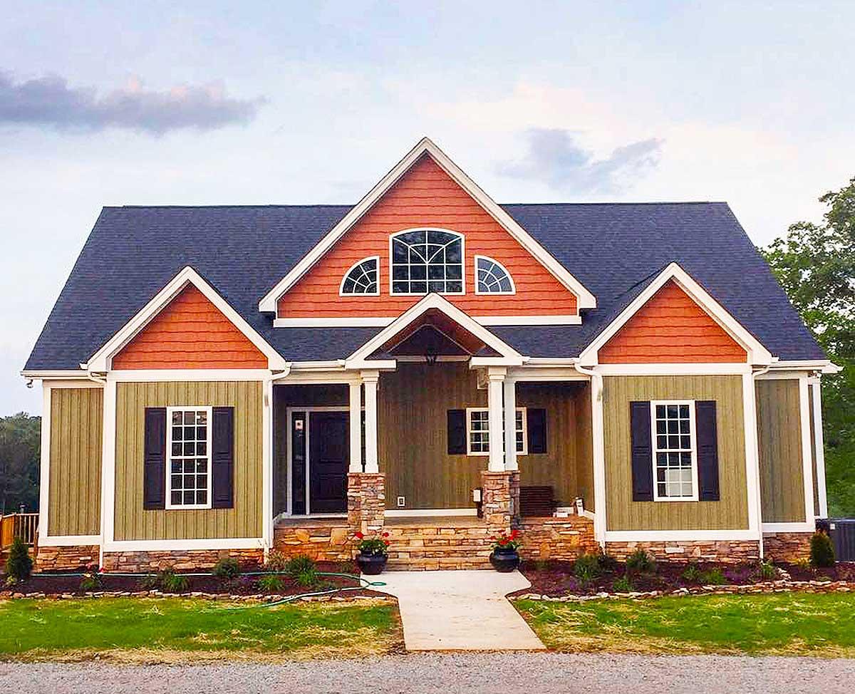 House plan exterior with two stories. Features include a gable roof, covered porch with columns, and decorative dormers with arched windows.