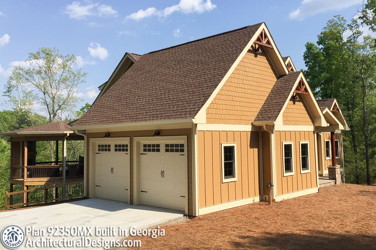 House plan exterior showing a two-car garage with wood trim gables and a covered porch with railing.