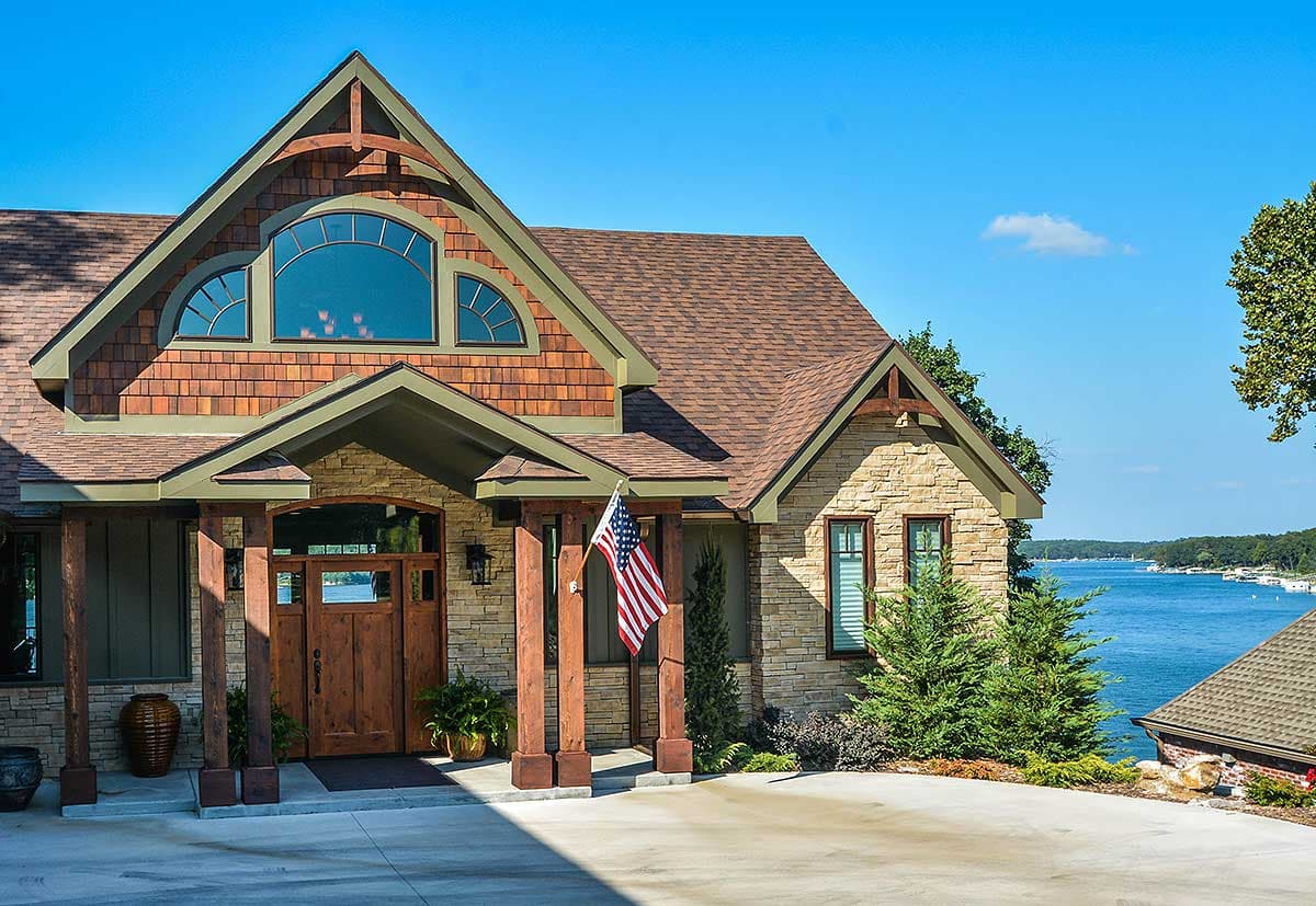 House plan exterior with stone and cedar siding, covered entry with timber posts, and arched window.