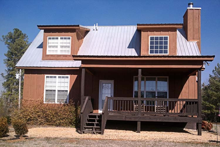 House plan exterior: Two-story cabin style with metal roof, dormers, and wrap-around porch.
