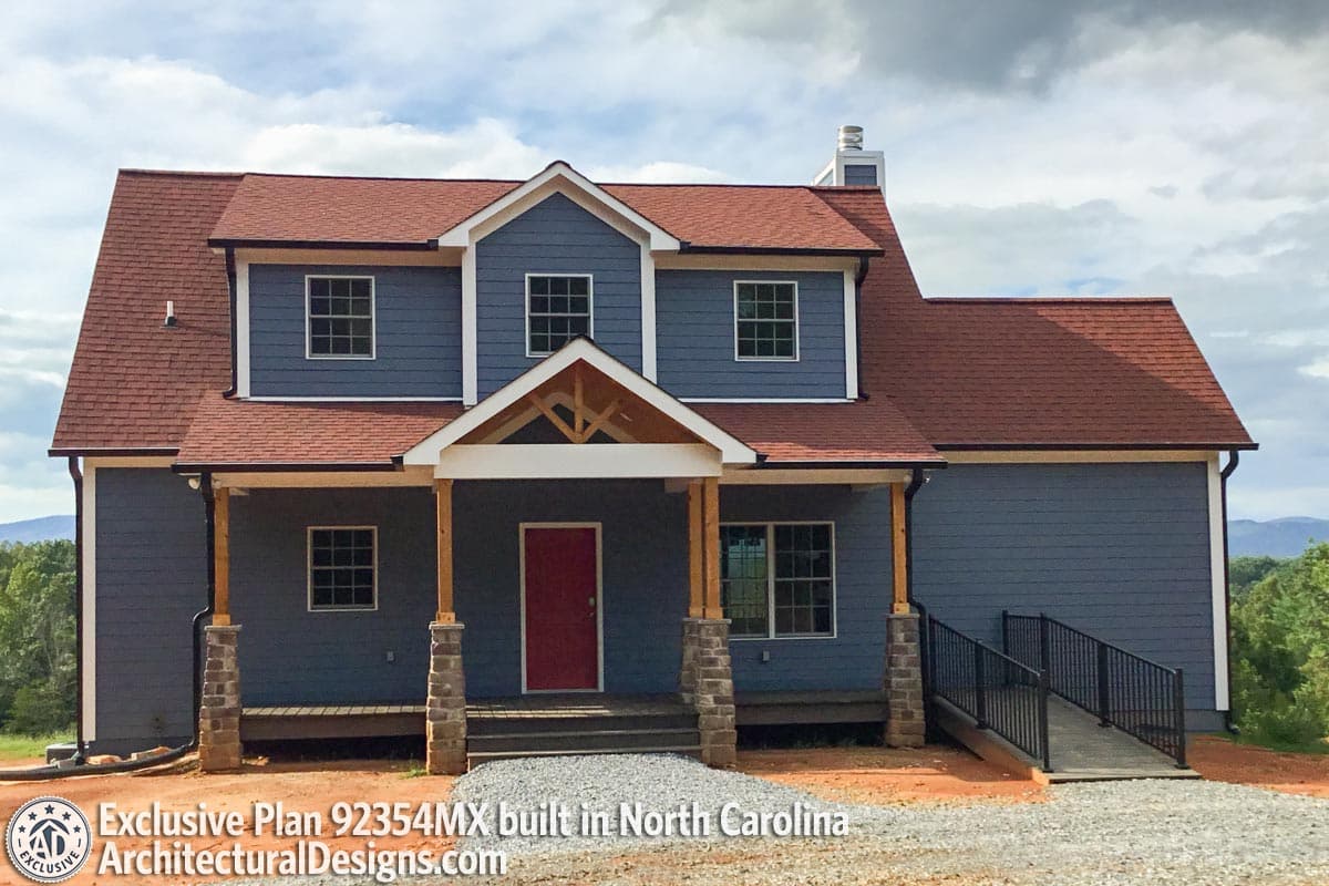 Two-story house plan exterior with a covered front porch, stone-clad posts, gabled dormer, and red roof.