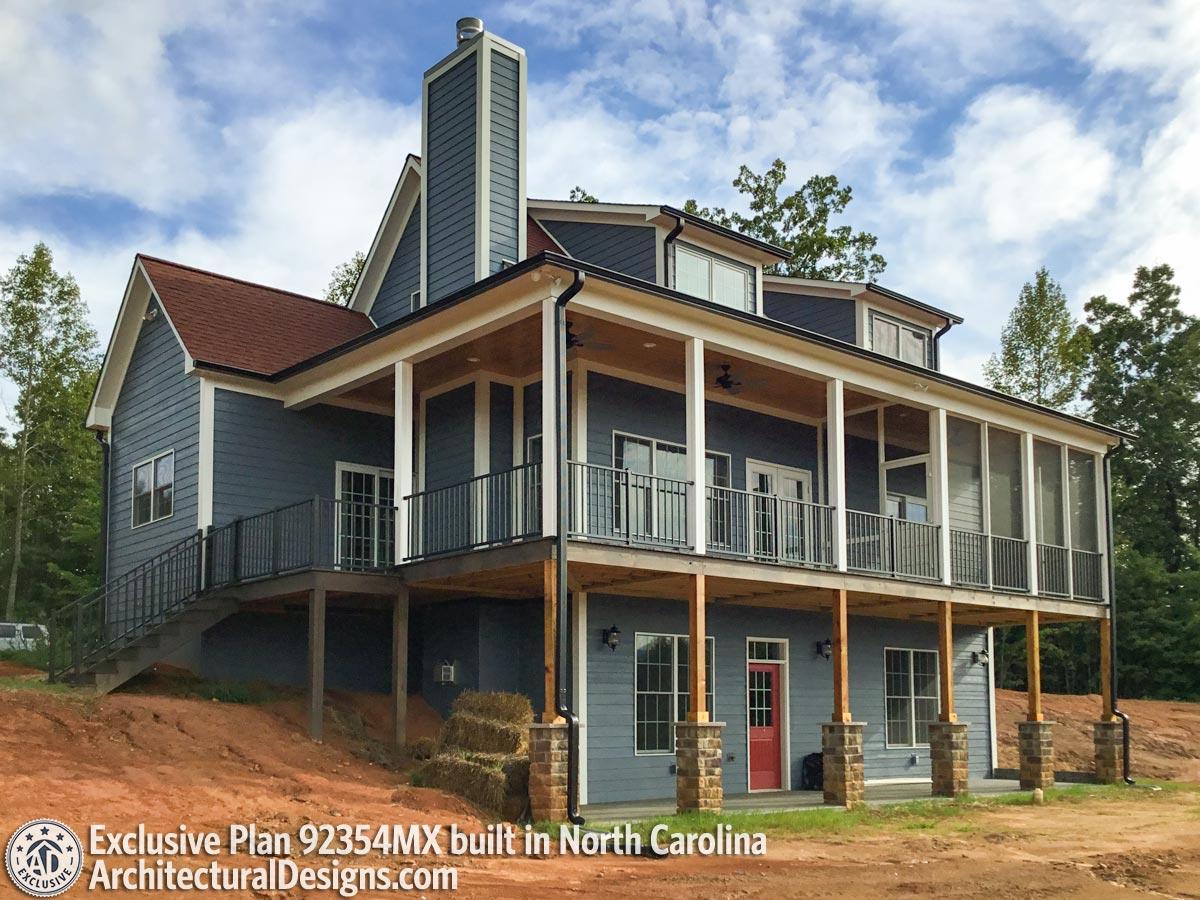 House plan exterior: Blue two-story home with a prominent chimney, wrap-around covered porch, and a screened-in section.