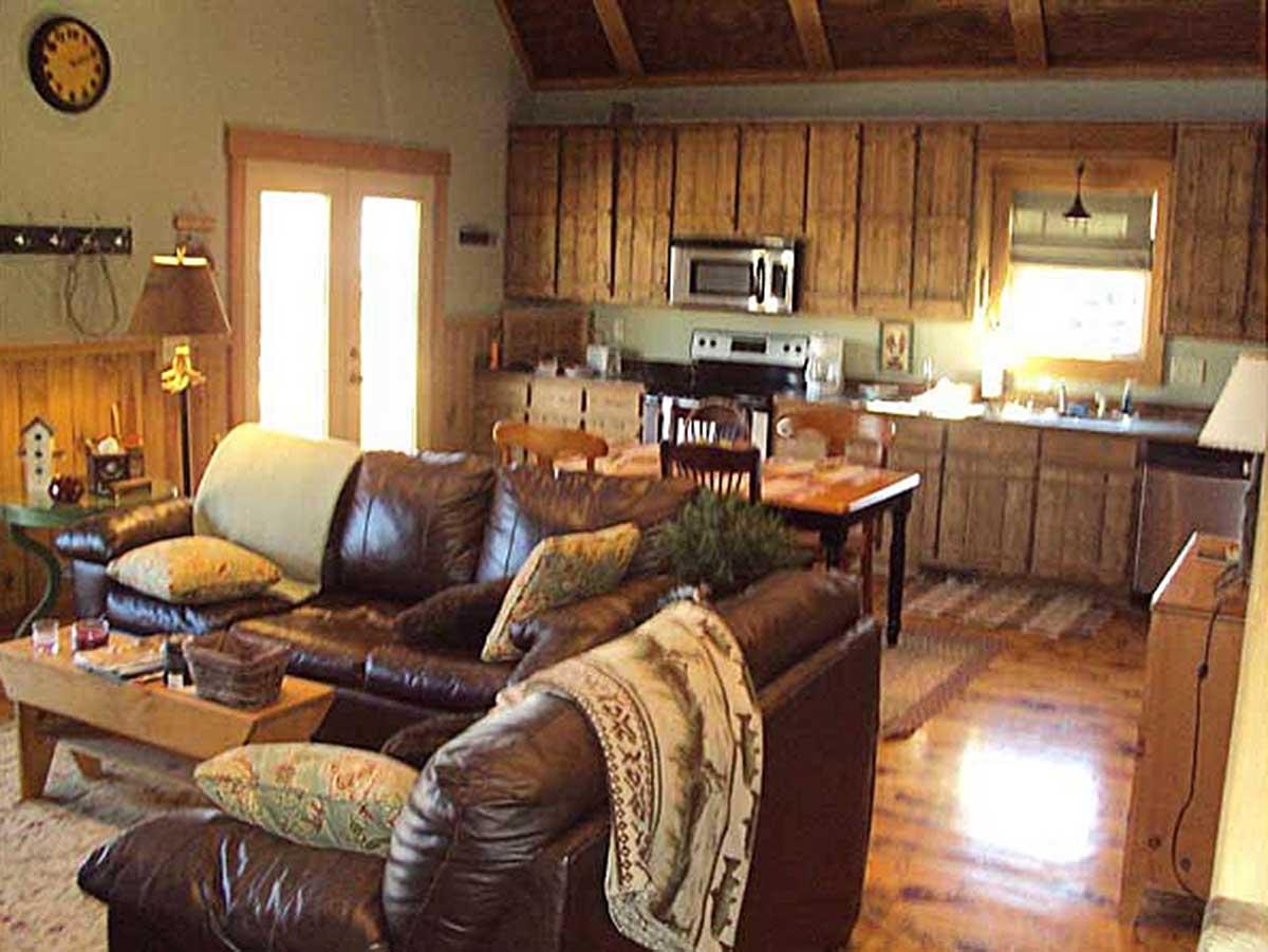 Living area and kitchen with dark leather sofas, wood cabinetry, stainless steel appliances, and beamed ceiling.