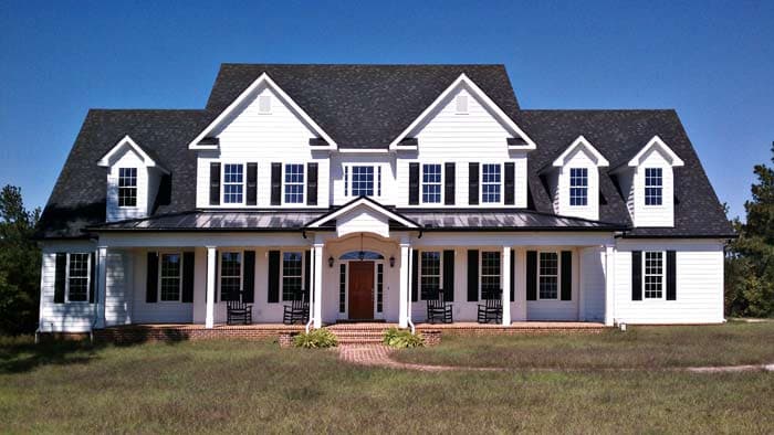 House plan exterior: Two-story white home with a wraparound porch, dormers, and multiple gables.