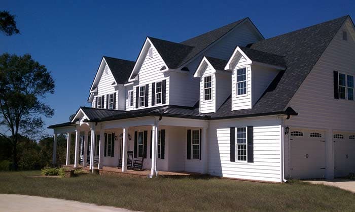 House plan exterior: Two-story Modern Farmhouse with wraparound porch, dormers, gables, and a three-car garage.