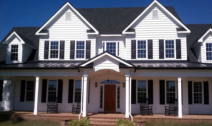 House plan exterior: Two-story white siding home with a wraparound porch, gables, dormers, and a metal roof.