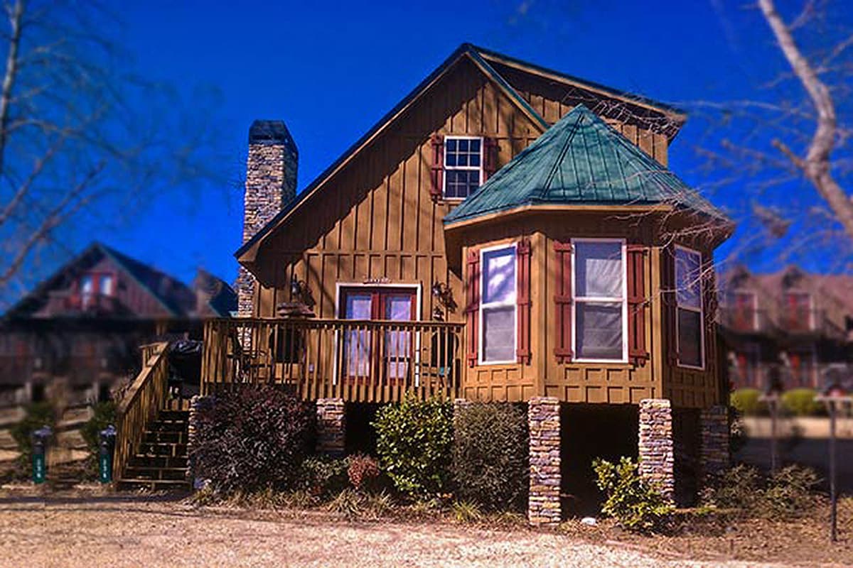 House plan exterior featuring wood siding, stone foundation, deck with railing, and a bay window with a conical roof.