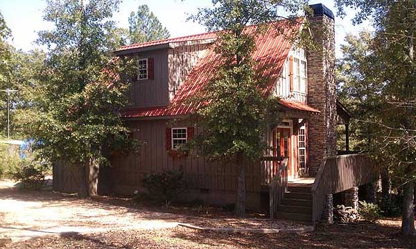 Two-story house plan exterior with rustic wood siding, red metal roof, stone chimney, and wrap-around porch.
