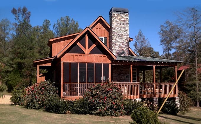 House plan exterior: Two-story dwelling with wood siding, screened porch, stone chimney, and wrap-around deck.
