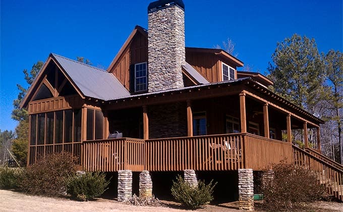 House plan exterior featuring a metal roof, stone chimney, wrap-around porch, and screened-in section.