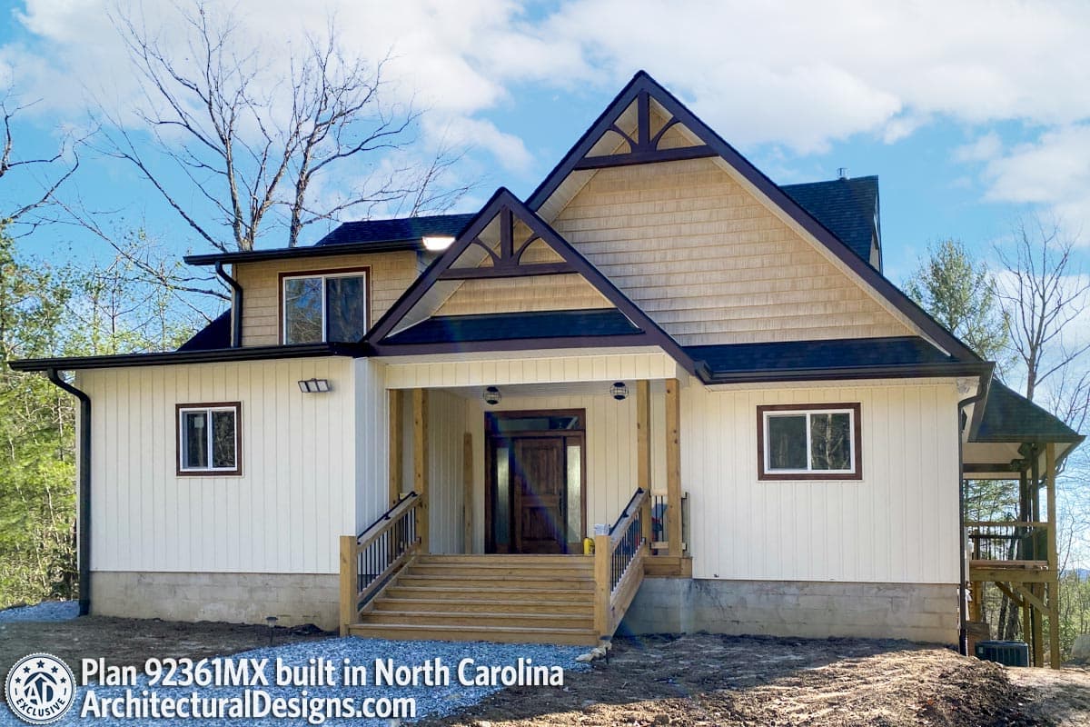 House plan exterior: Two-story home with prominent gables, wood shake siding, covered front porch with wooden beams, and a wide staircase.