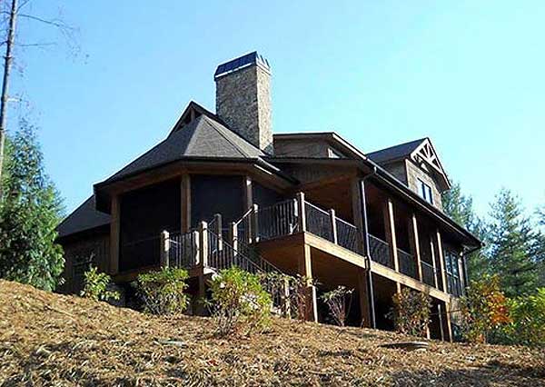House plan exterior with stone chimney, screened porch, wrap-around deck, and multiple gables. Two stories visible.