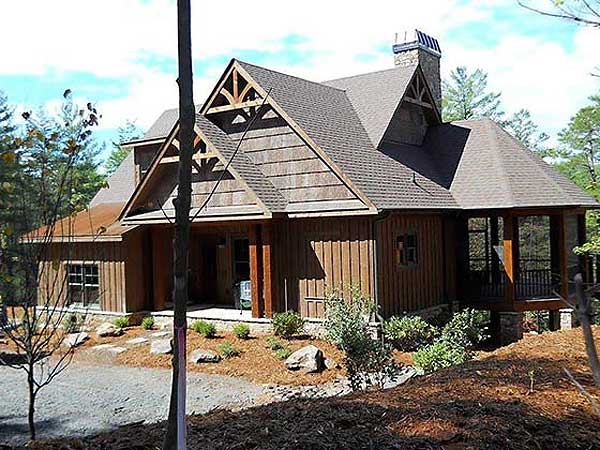 House plan exterior: Modern lodge style with exposed rafter tails, wood siding, stone chimney, and covered porch.