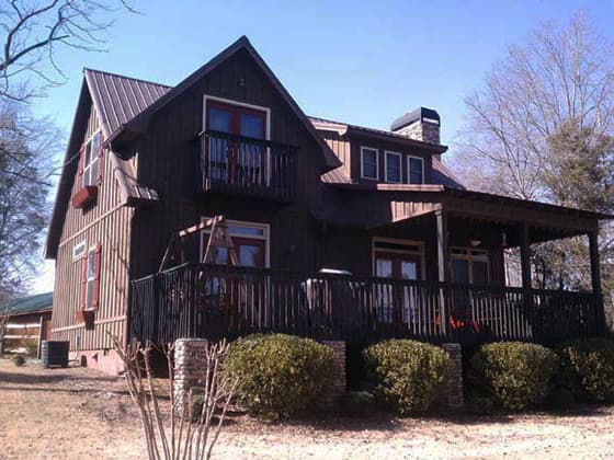 House plan exterior: Two-story cabin-style home with metal roof, wrap-around porch, and upper-level balconies.