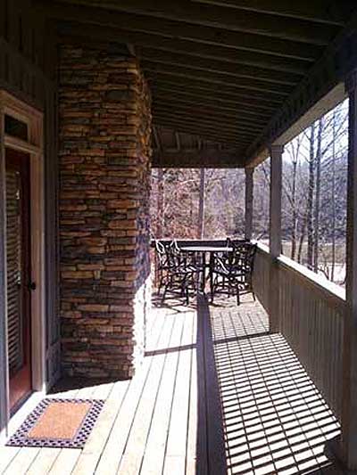 Covered porch with stone chimney, wooden deck, and outdoor dining set.
