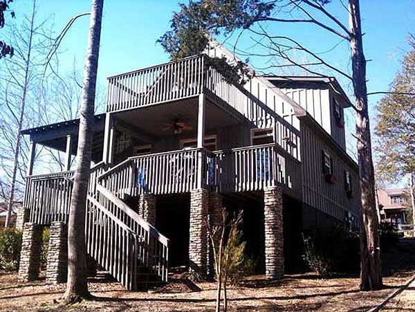 House plan exterior of a two-story home with stone foundation piers, wraparound decks, and a prominent central staircase.