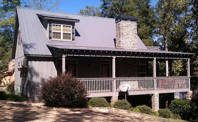 House plan exterior: two-story, metal roof, stone chimney, and wrap-around porch with railings.
