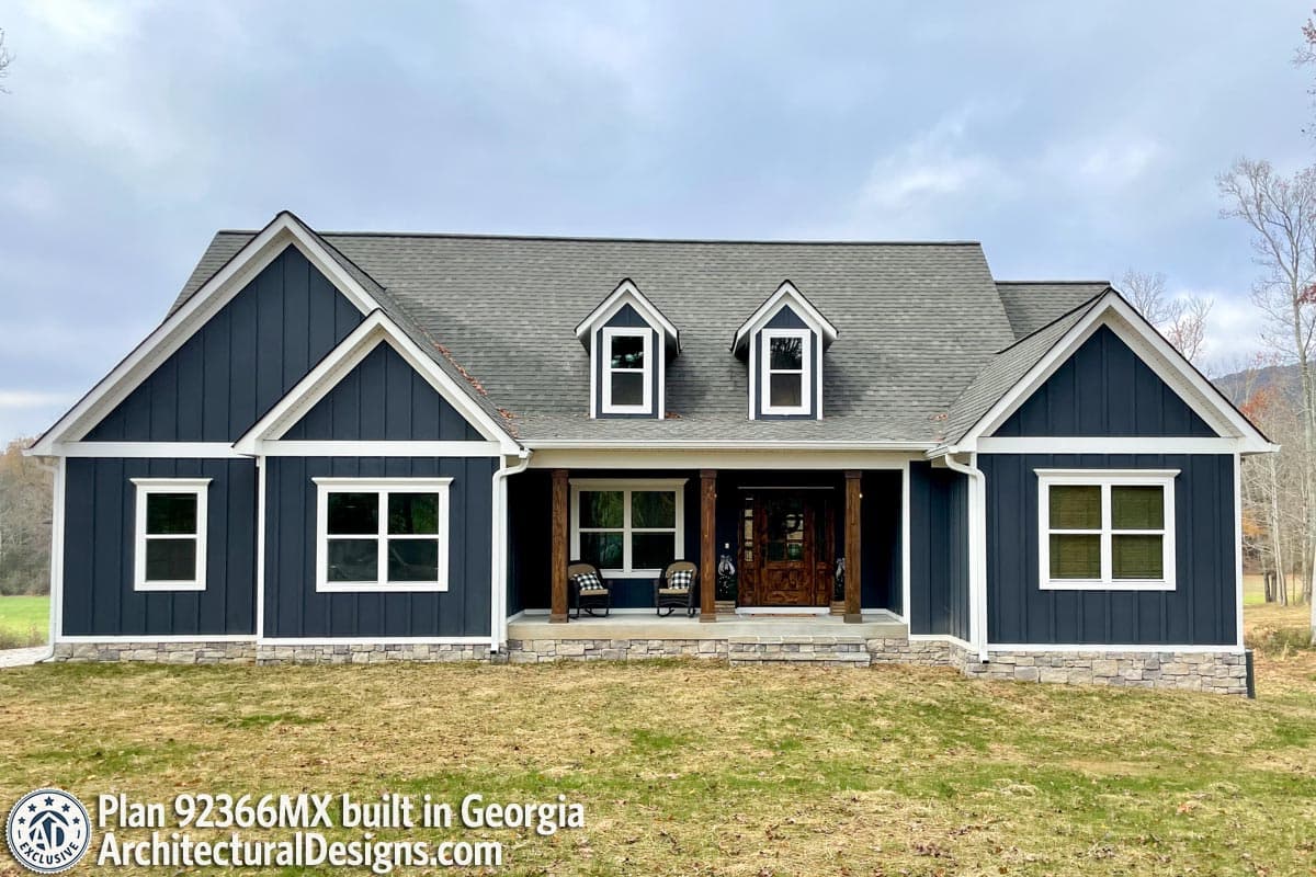 House plan exterior: Modern Farmhouse style, one-story with gables, dormers, stone foundation, and covered porch with wood columns.
