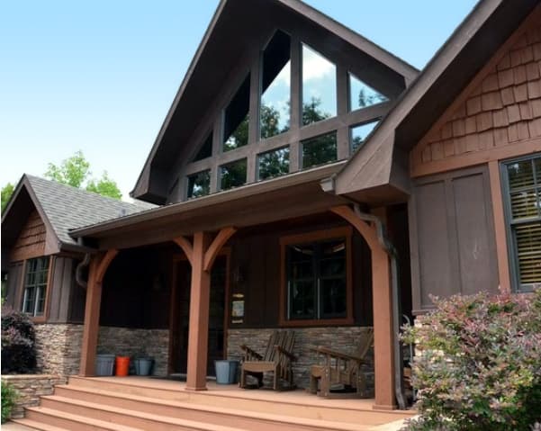 House plan exterior with stone foundation, wooden posts supporting covered porch, and a tall, multi-pane window wall.