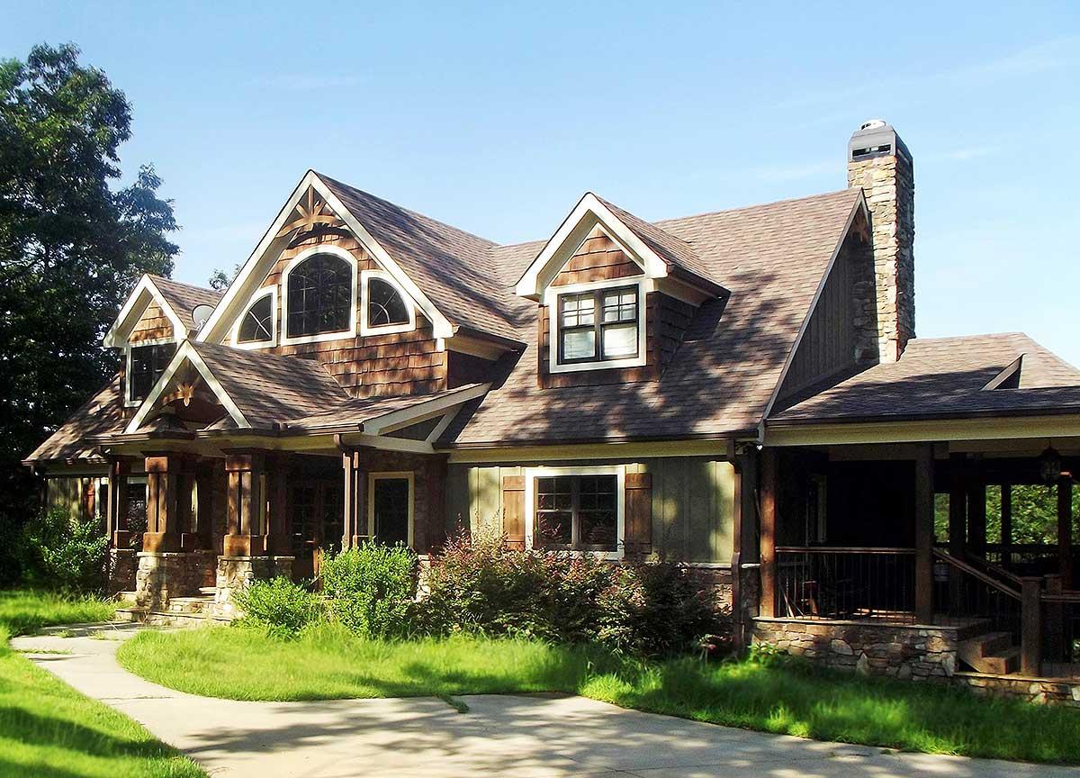 House plan exterior with natural wood siding, stone accents, prominent gables, arched dormer windows, and covered porch.