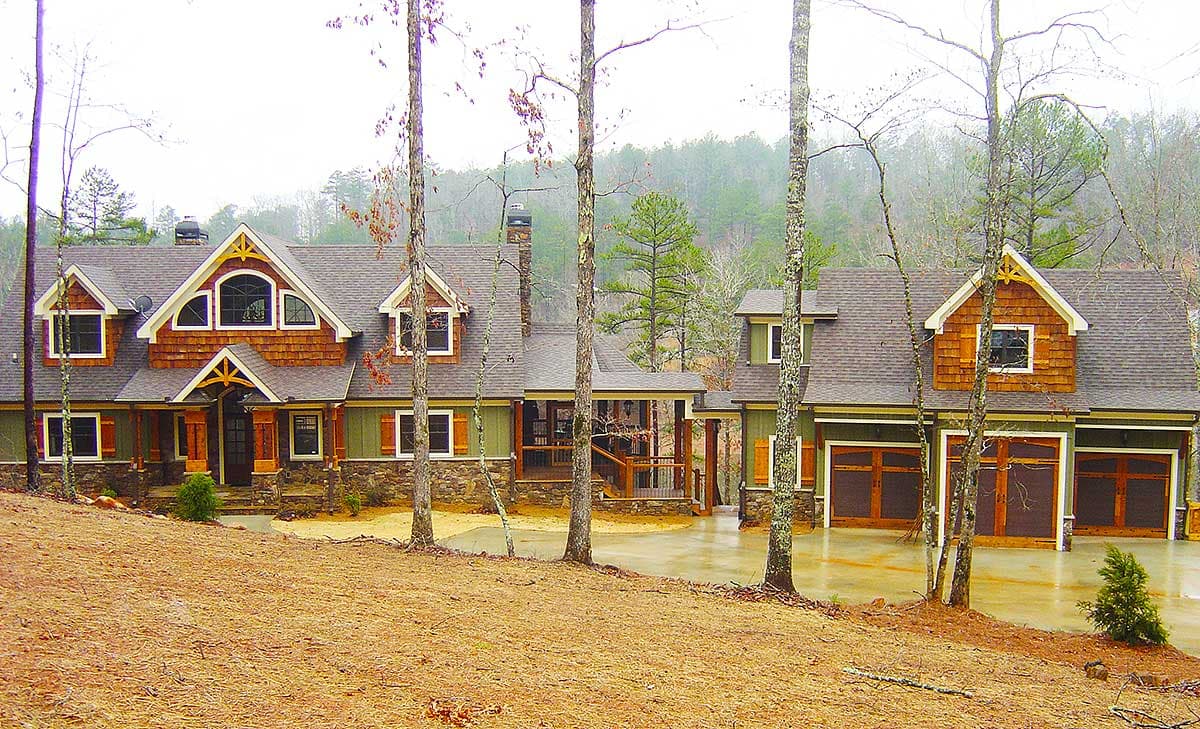 House plan exterior: Two-story lodge style with shingle siding, prominent gables, covered porch, and three-car garage.