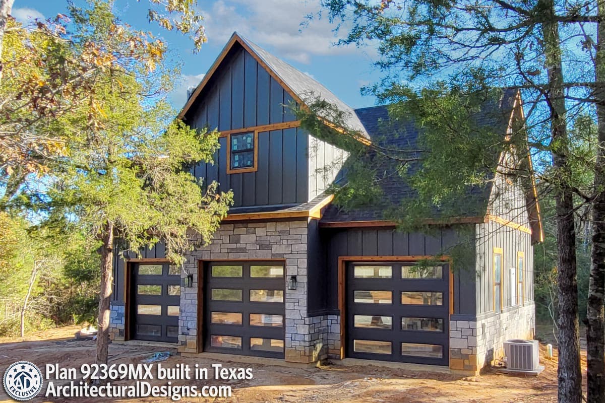 House plan exterior: Modern style with stone base, vertical siding, and three glass garage doors.