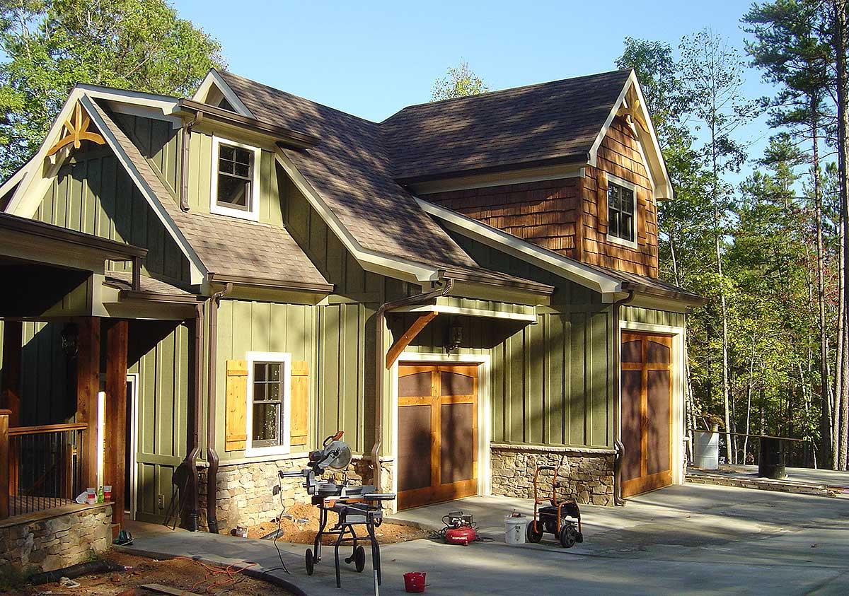 Craftsman style house plan exterior with board and batten siding, stone foundation, multiple gables, dormers, and wood garage doors.