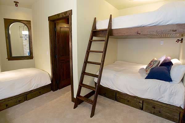Bedroom interior with bunk beds, single bed, wooden ladder, and arched mirror over single bed.