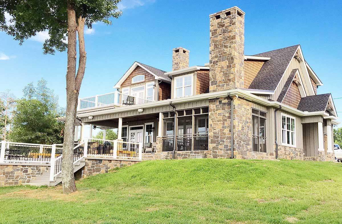 House plan exterior with stone facade, multiple gables, stone chimneys, and wrap-around porch.