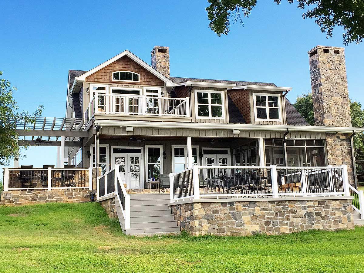 House plan exterior of a two-story home with stone foundation, wraparound porch, dormers, and dual stone chimneys.