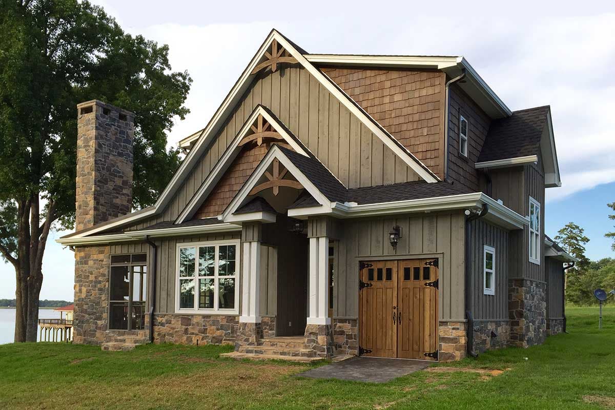 Craftsman style house plan exterior with stone foundation, wood siding, steep gables, decorative brackets, and a wooden garage door.