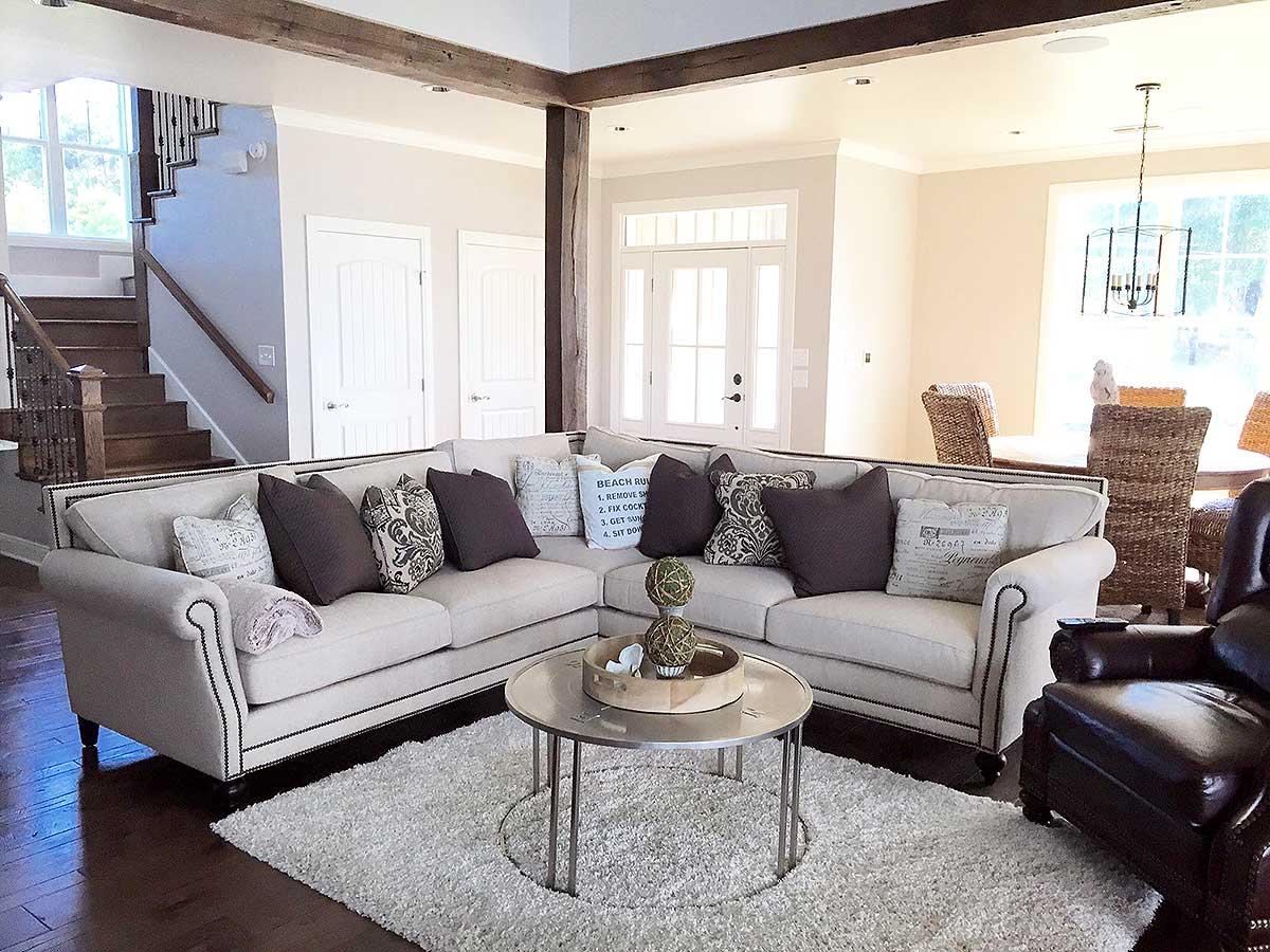 Living room with sectional sofa, coffee table, rug, fireplace, stairs, and dining area. Exposed wooden beams overhead.